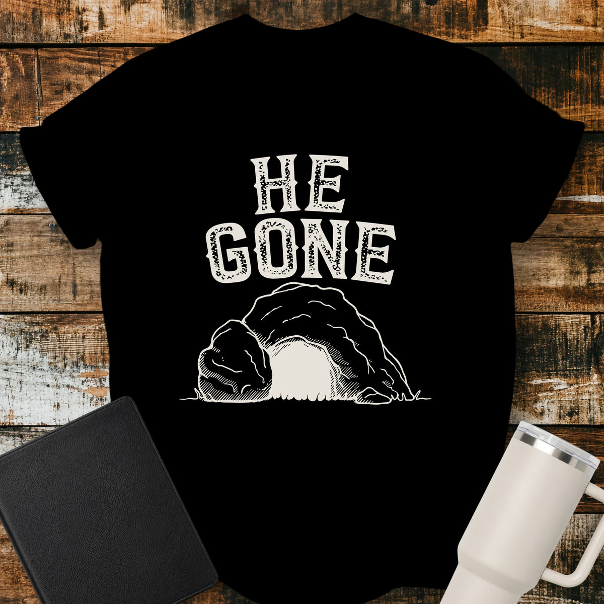 black Christian T-shirt featuring an empty tomb illustration with the words “He Gone” in distressed cream lettering.