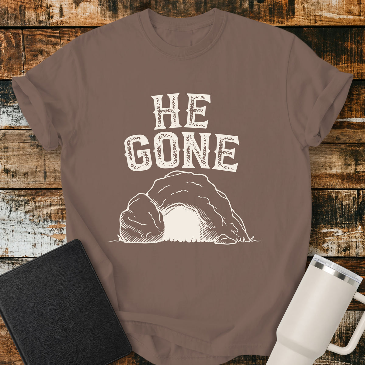 espresso brown Christian T-shirt featuring an empty tomb illustration with the words “He Gone” in distressed cream lettering.