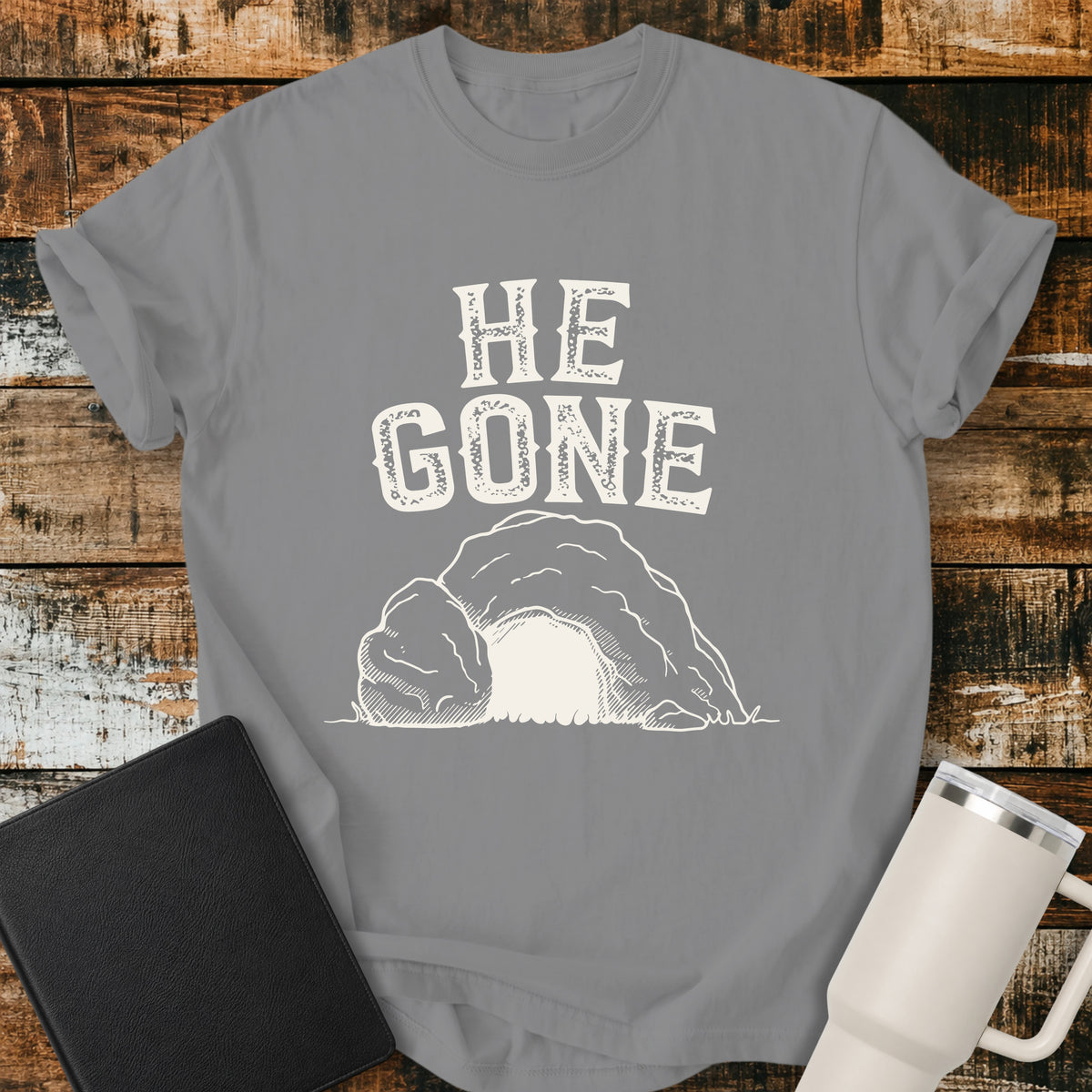 grey Christian T-shirt featuring an empty tomb illustration with the words “He Gone” in distressed cream lettering.