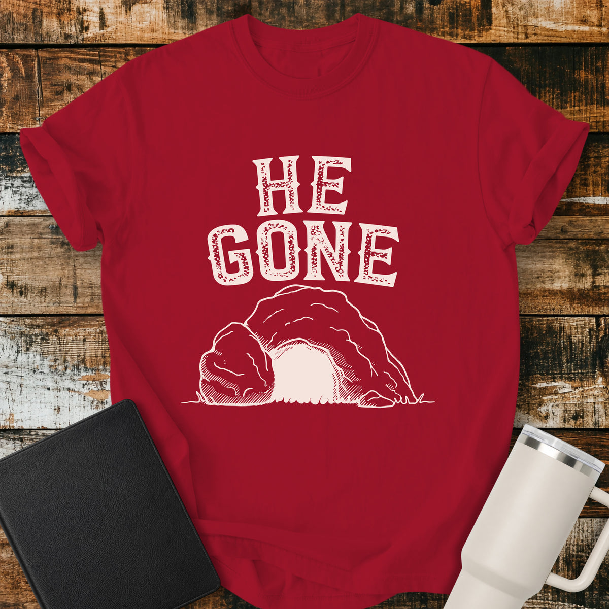 red Christian T-shirt featuring an empty tomb illustration with the words “He Gone” in distressed cream lettering.