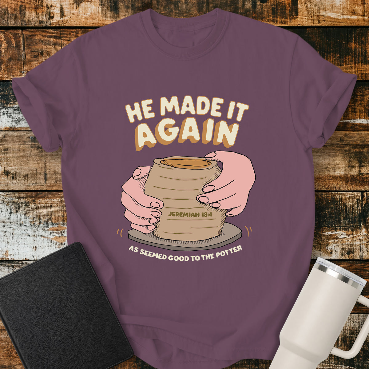 berry purple Christian t-shirt featuring hands shaping a clay vessel on a potter’s wheel, with the phrase “He Made It Again,” Jeremiah 18:4, and “As Seemed Good to the Potter.” A retro-inspired biblical design illustrating God as the Potter.