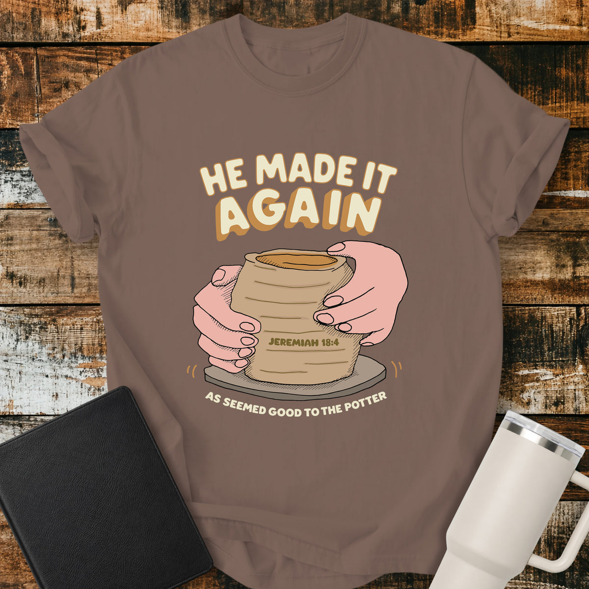 espresso brown Christian t-shirt featuring hands shaping a clay vessel on a potter’s wheel, with the phrase “He Made It Again,” Jeremiah 18:4, and “As Seemed Good to the Potter.” A retro-inspired biblical design illustrating God as the Potter.