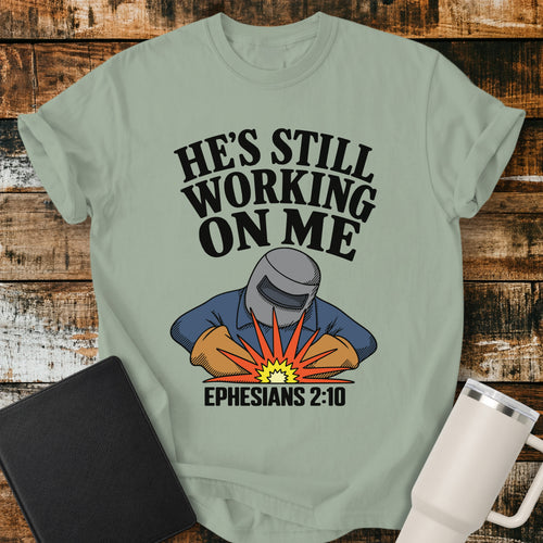 bay green Christian t-shirt featuring a vintage welder illustration with bold retro lettering reading “He’s Still Working on Me” and Ephesians 2:10.