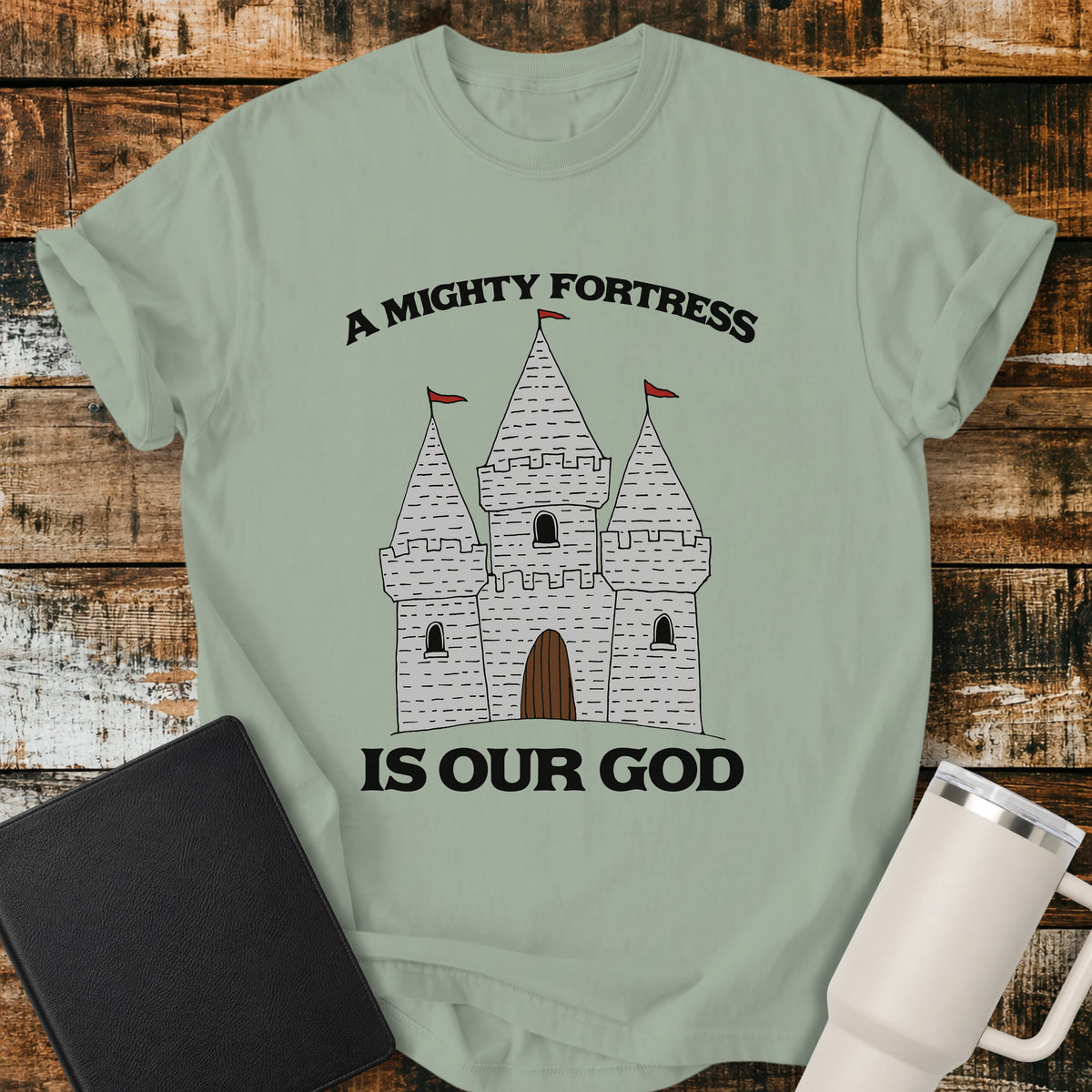bay green Christian t-shirt featuring a hand-drawn castle illustration with bold vintage lettering reading “A Mighty Fortress Is Our God.”