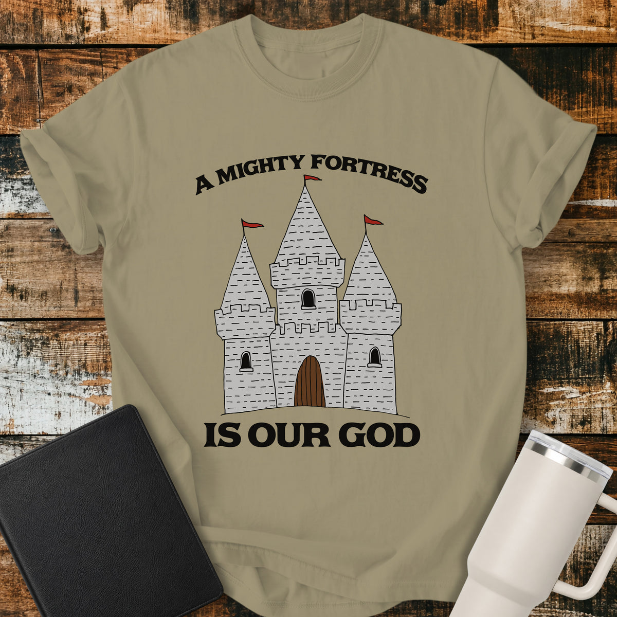 khaki Christian t-shirt featuring a hand-drawn castle illustration with bold vintage lettering reading “A Mighty Fortress Is Our God.”
