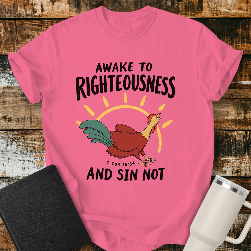 crunchberry pink graphic T-shirt mockup featuring a rooster illustration with a rising sun and the phrase “Awake to Righteousness and Sin Not” with a 1 Corinthians 15:34 reference, styled with a black Bible and white tumbler on a rustic wood background.
