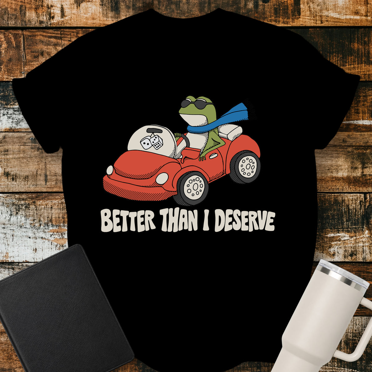 black Christian T-shirt featuring a frog driving a red convertible with the words “Better Than I Deserve” in cream retro lettering.