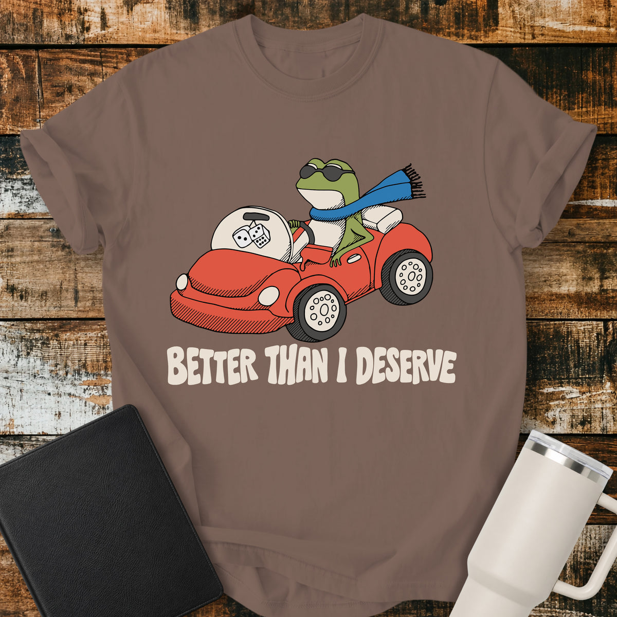 espresso brown Christian T-shirt featuring a frog driving a red convertible with the words “Better Than I Deserve” in cream retro lettering.