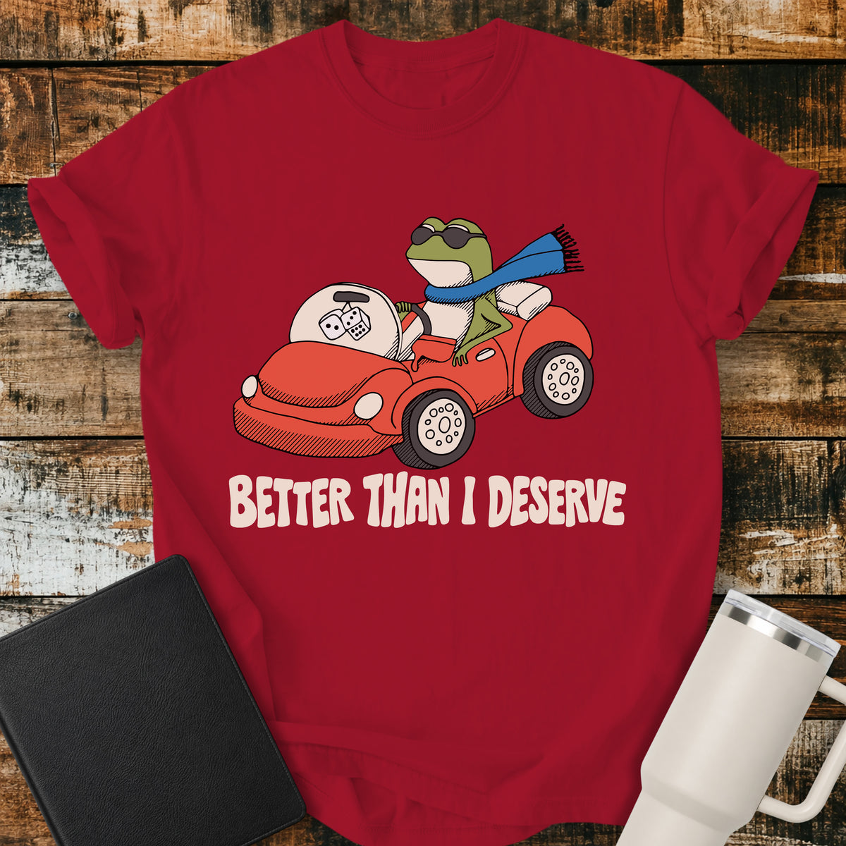 red Christian T-shirt featuring a frog driving a red convertible with the words “Better Than I Deserve” in cream retro lettering.