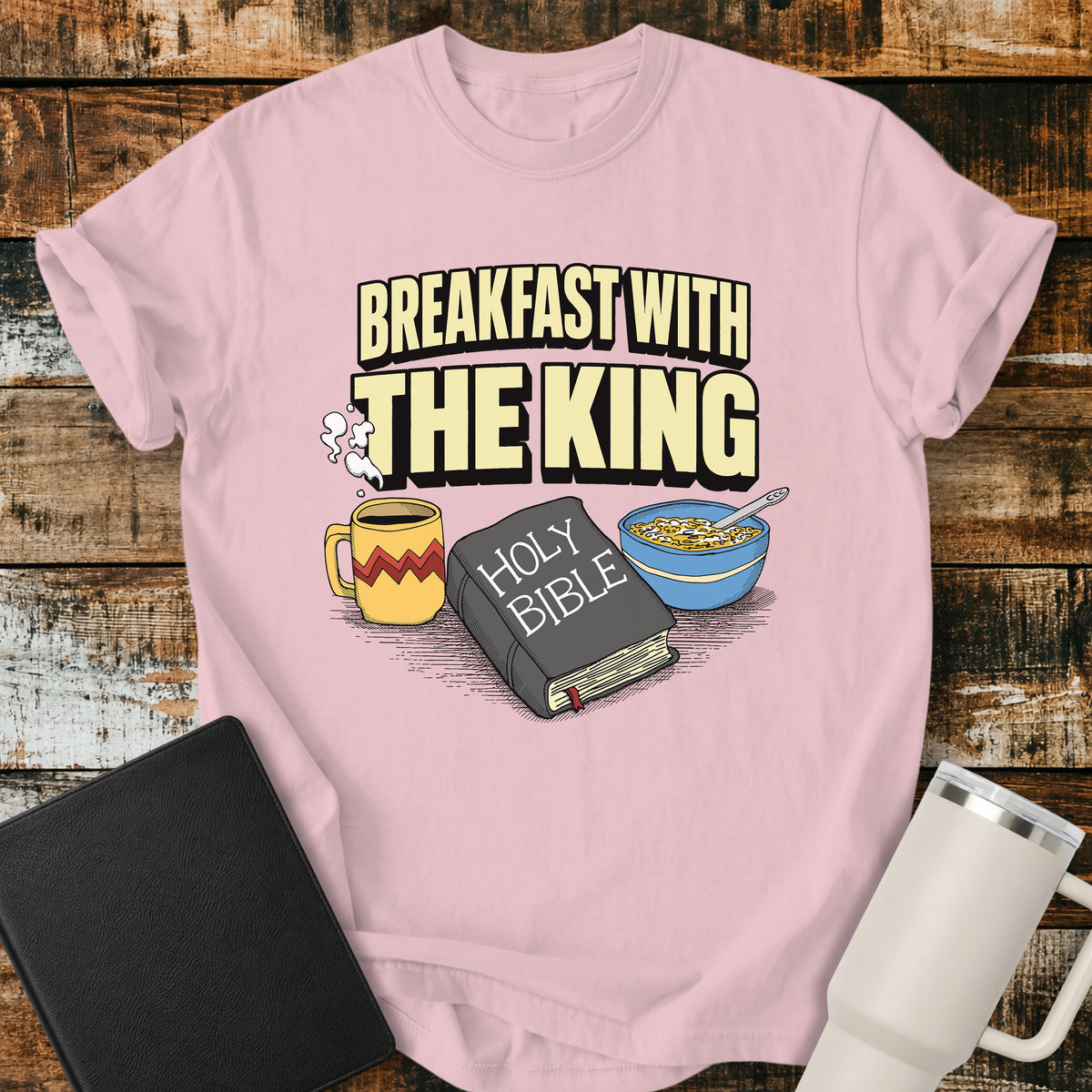 blossom pink Christian t-shirt featuring the phrase “Breakfast With the King” above a retro illustrated Holy Bible, steaming coffee mug, and bowl of cereal. A colorful vintage-inspired faith design with a fun breakfast theme.