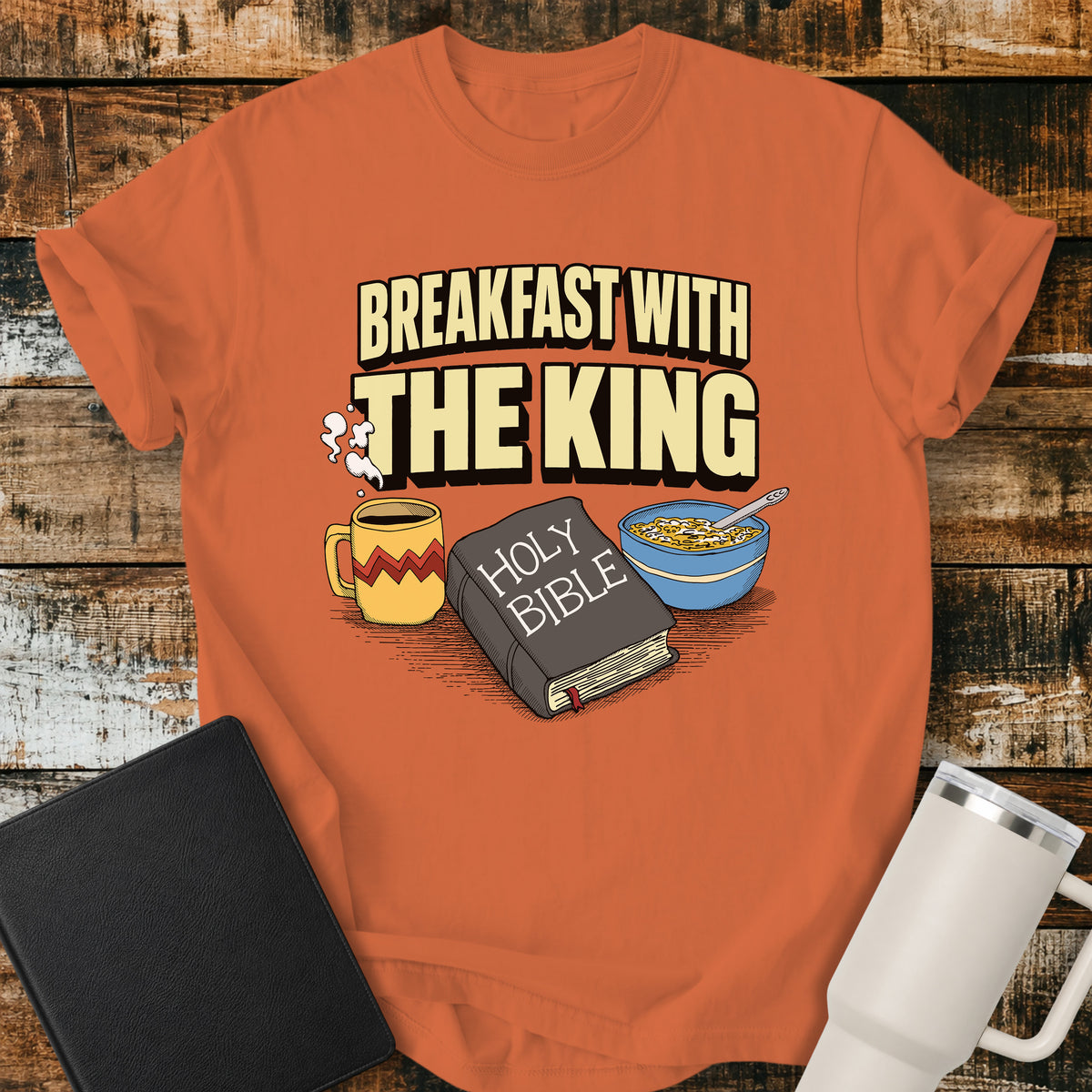 burnt orange Christian t-shirt featuring the phrase “Breakfast With the King” above a retro illustrated Holy Bible, steaming coffee mug, and bowl of cereal. A colorful vintage-inspired faith design with a fun breakfast theme.