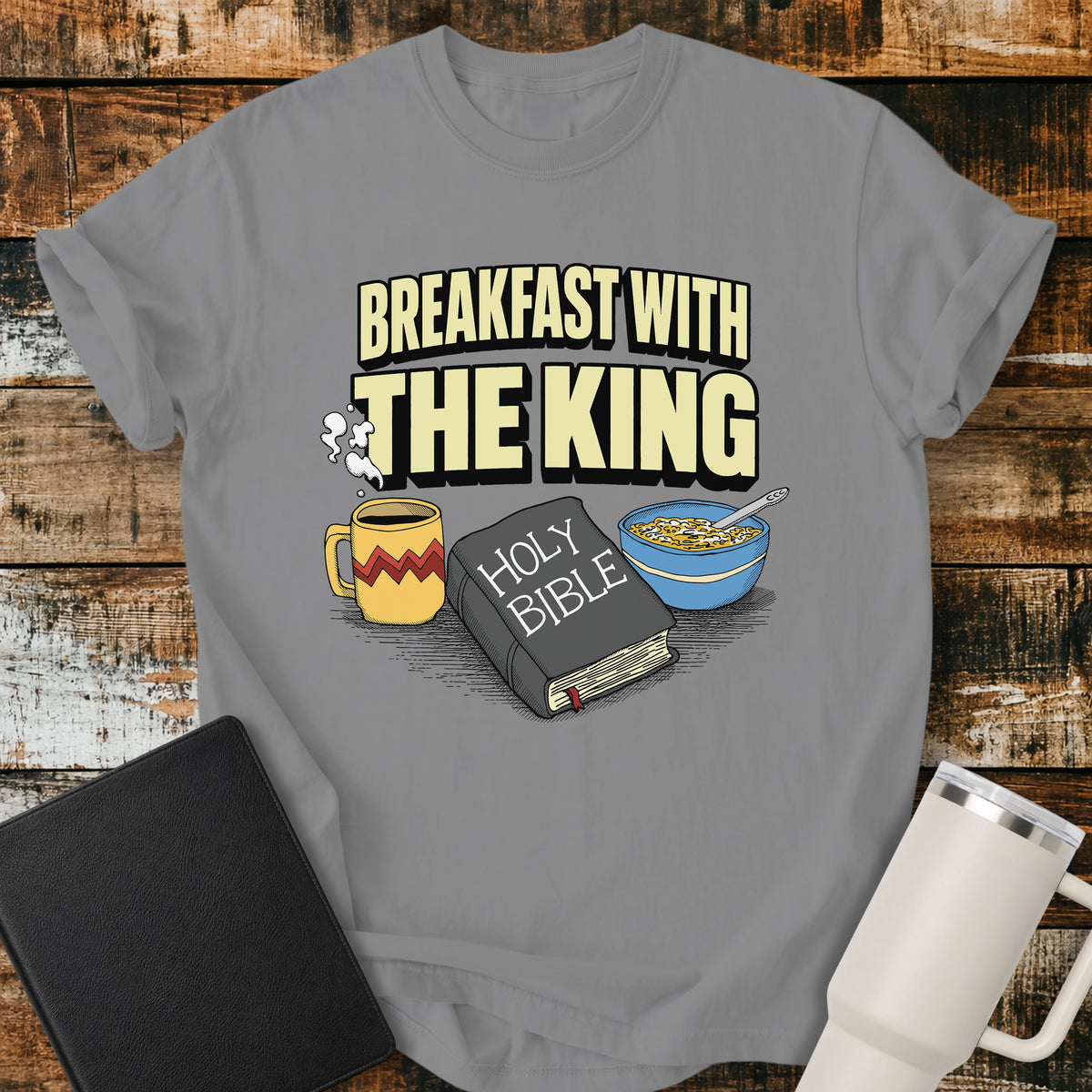 grey Christian t-shirt featuring the phrase “Breakfast With the King” above a retro illustrated Holy Bible, steaming coffee mug, and bowl of cereal. A colorful vintage-inspired faith design with a fun breakfast theme.