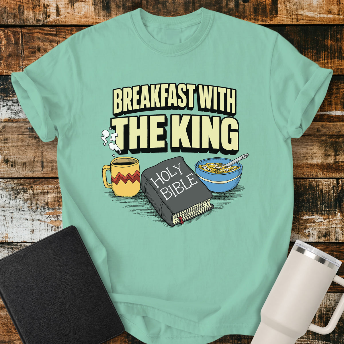 Island Reef green Christian t-shirt featuring the phrase “Breakfast With the King” above a retro illustrated Holy Bible, steaming coffee mug, and bowl of cereal. A colorful vintage-inspired faith design with a fun breakfast theme.