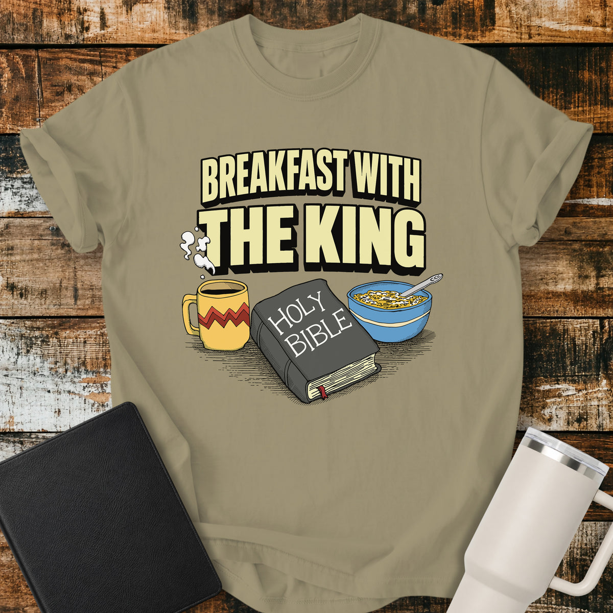 khaki Christian t-shirt featuring the phrase “Breakfast With the King” above a retro illustrated Holy Bible, steaming coffee mug, and bowl of cereal. A colorful vintage-inspired faith design with a fun breakfast theme.