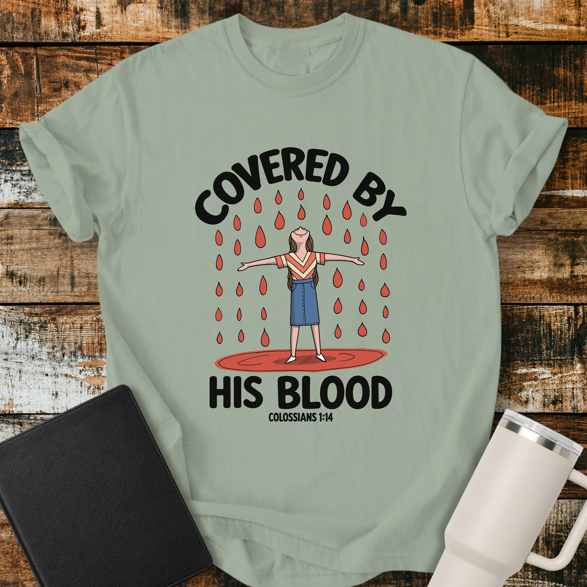 bay green Christian t-shirt featuring a woman standing beneath falling drops with the bold message “Covered By His Blood,” inspired by Colossians 1:14.