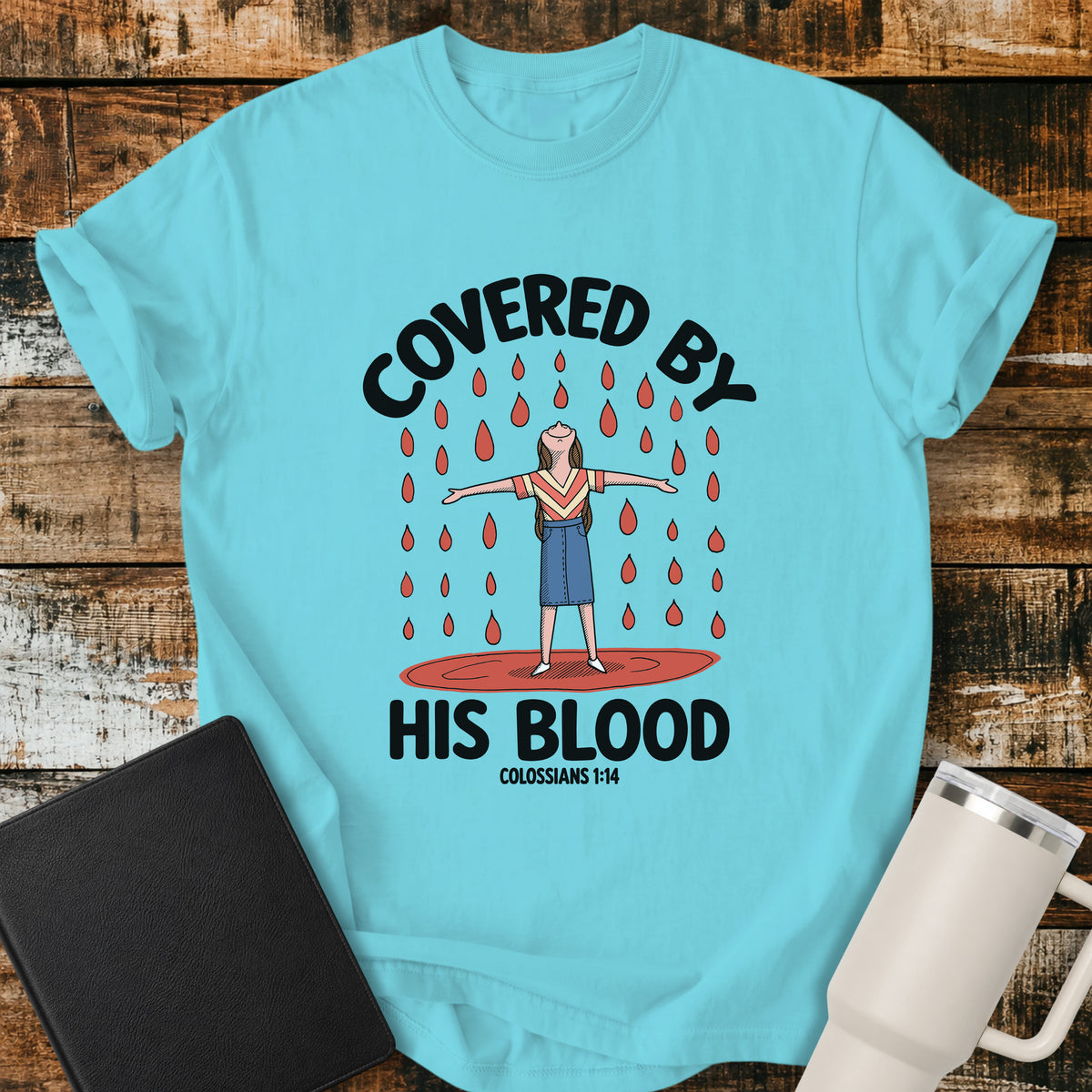 lagoon blue Christian t-shirt featuring a woman standing beneath falling drops with the bold message “Covered By His Blood,” inspired by Colossians 1:14.