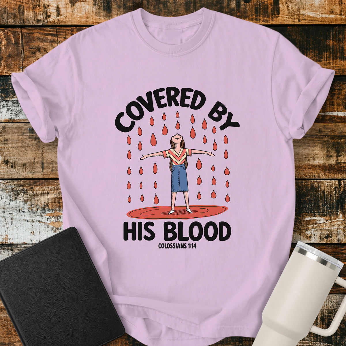 Orchid Christian t-shirt featuring a woman standing beneath falling drops with the bold message “Covered By His Blood,” inspired by Colossians 1:14.