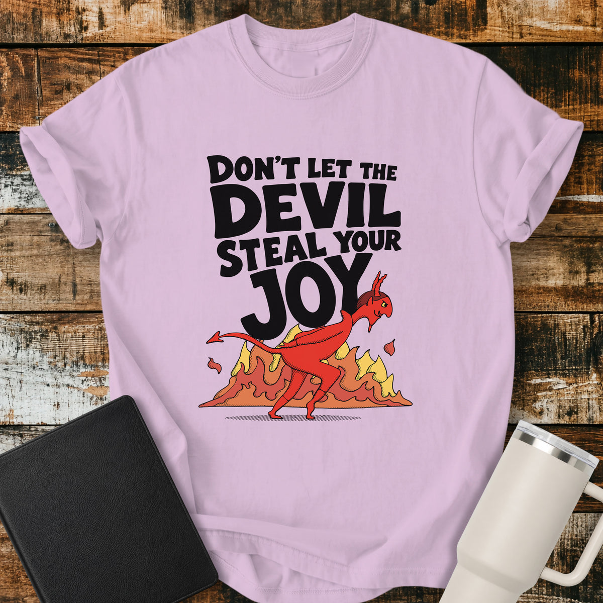 orchid purple Christian t-shirt featuring the bold phrase “Don’t Let the Devil Steal Your Joy” with a retro red devil sneaking away in front of stylized flames. A playful vintage-inspired faith design with bold black typography.