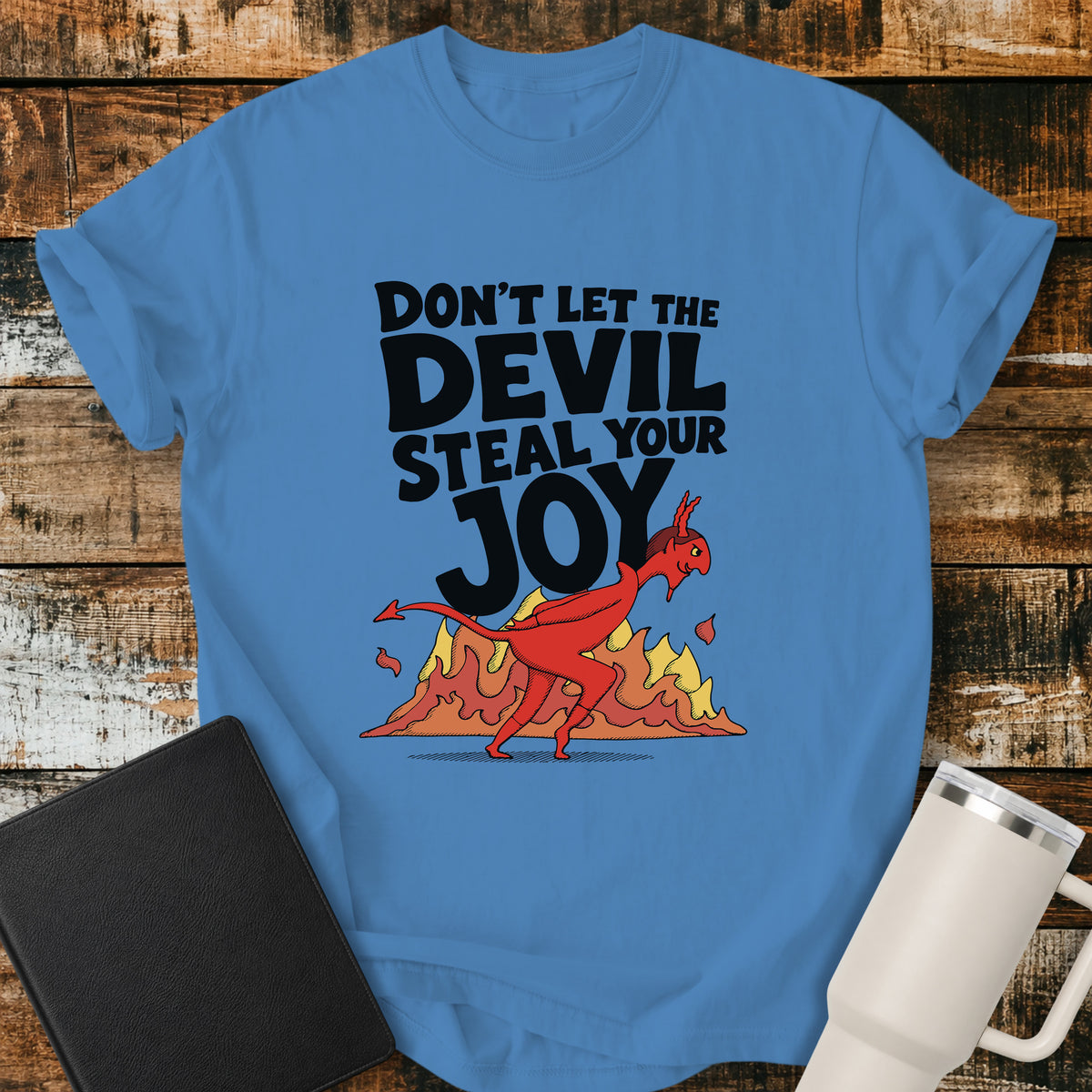 royal caribe blue Christian t-shirt featuring the bold phrase “Don’t Let the Devil Steal Your Joy” with a retro red devil sneaking away in front of stylized flames. A playful vintage-inspired faith design with bold black typography.
