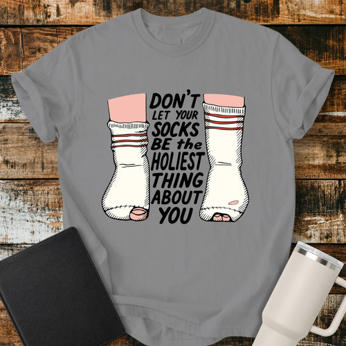 grey Christian T-shirt featuring worn, holey socks with the humorous phrase “Don’t Let Your Socks Be the Holiest Thing About You” in black lettering