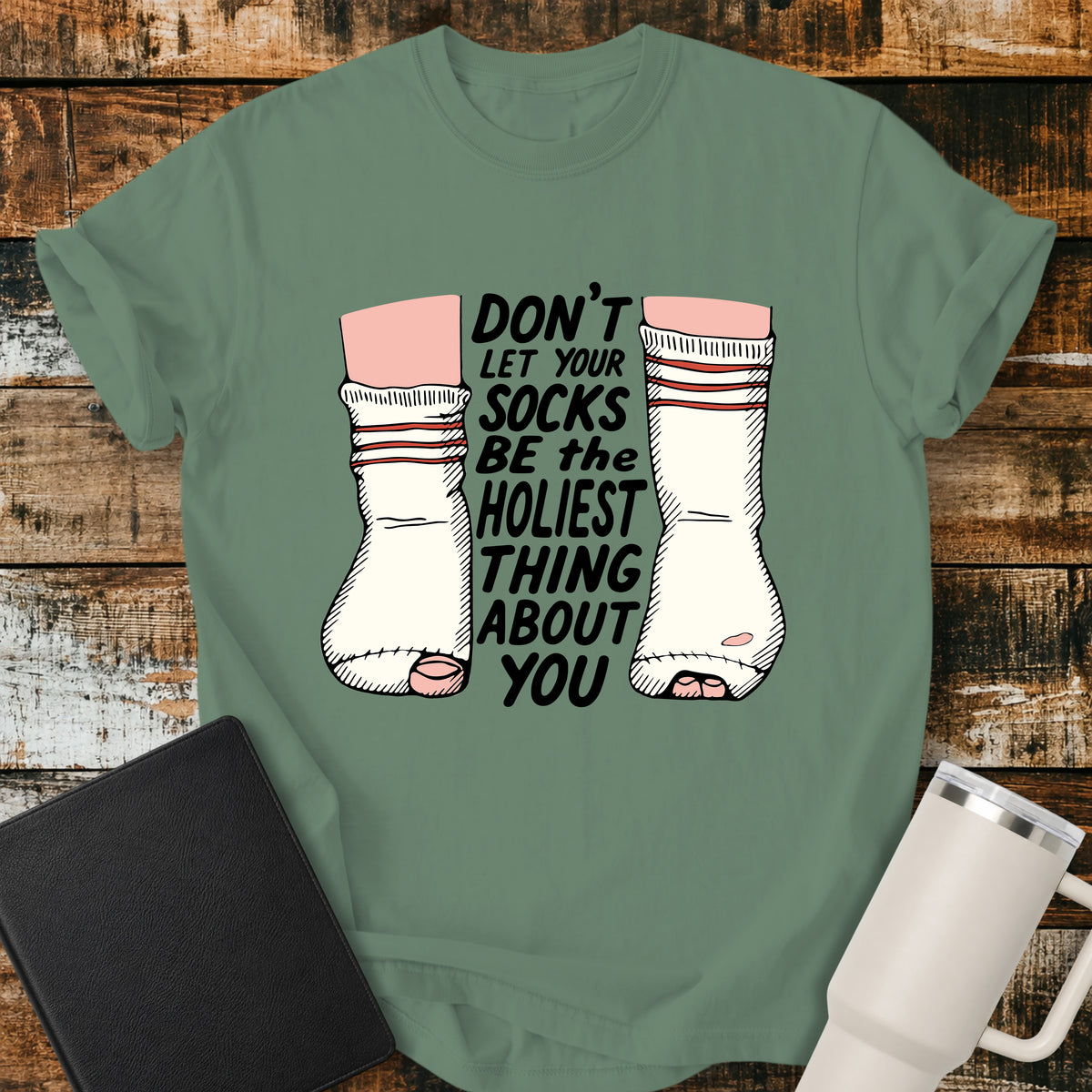 light green Christian T-shirt featuring worn, holey socks with the humorous phrase “Don’t Let Your Socks Be the Holiest Thing About You” in black lettering