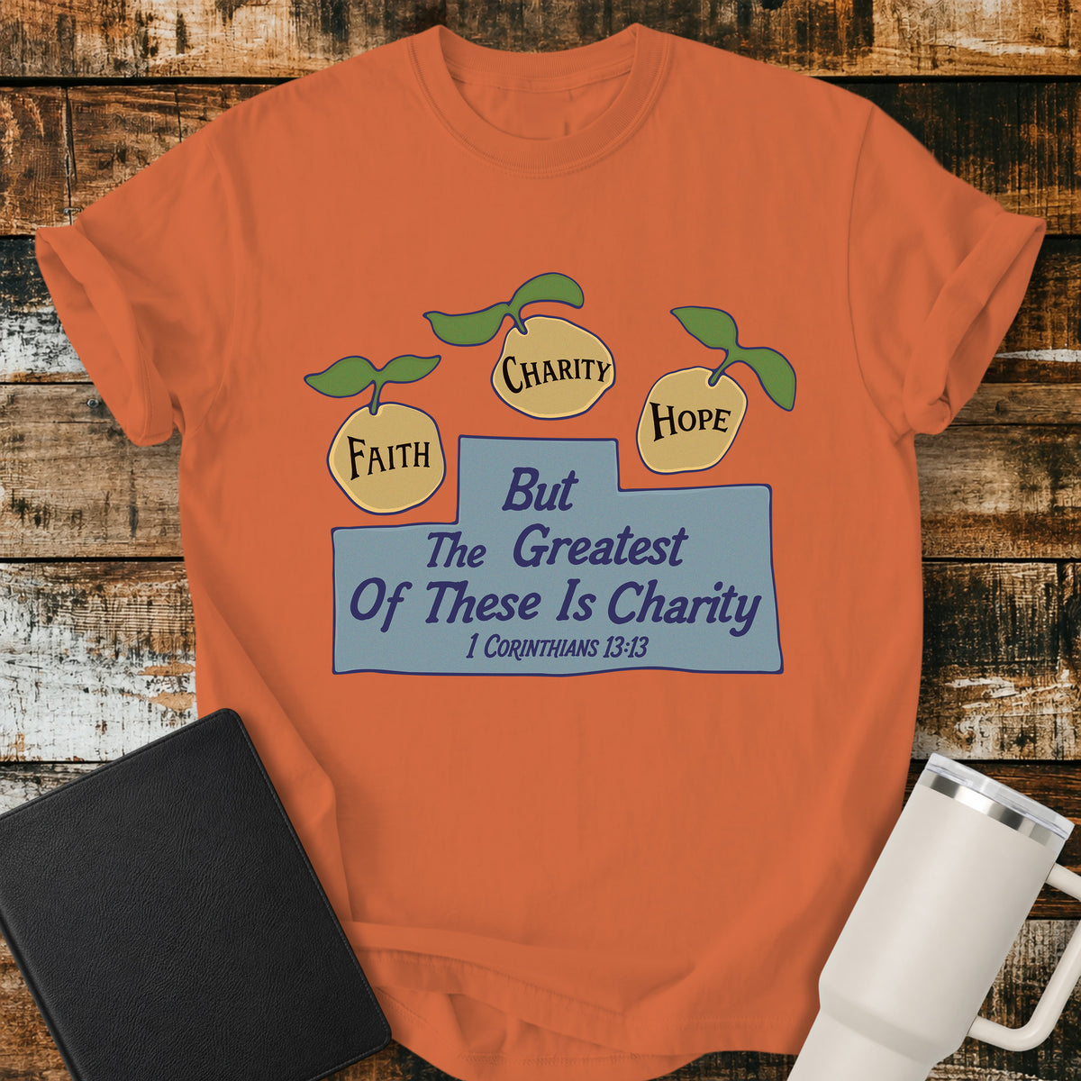 burnt orange Christian t-shirt featuring three lemons labeled “Faith,” “Charity,” and “Hope,” with the words “But the Greatest of These Is Charity” and 1 Corinthians 13:13. A cheerful, vintage-inspired biblical design illustrating faith, hope, and charity.