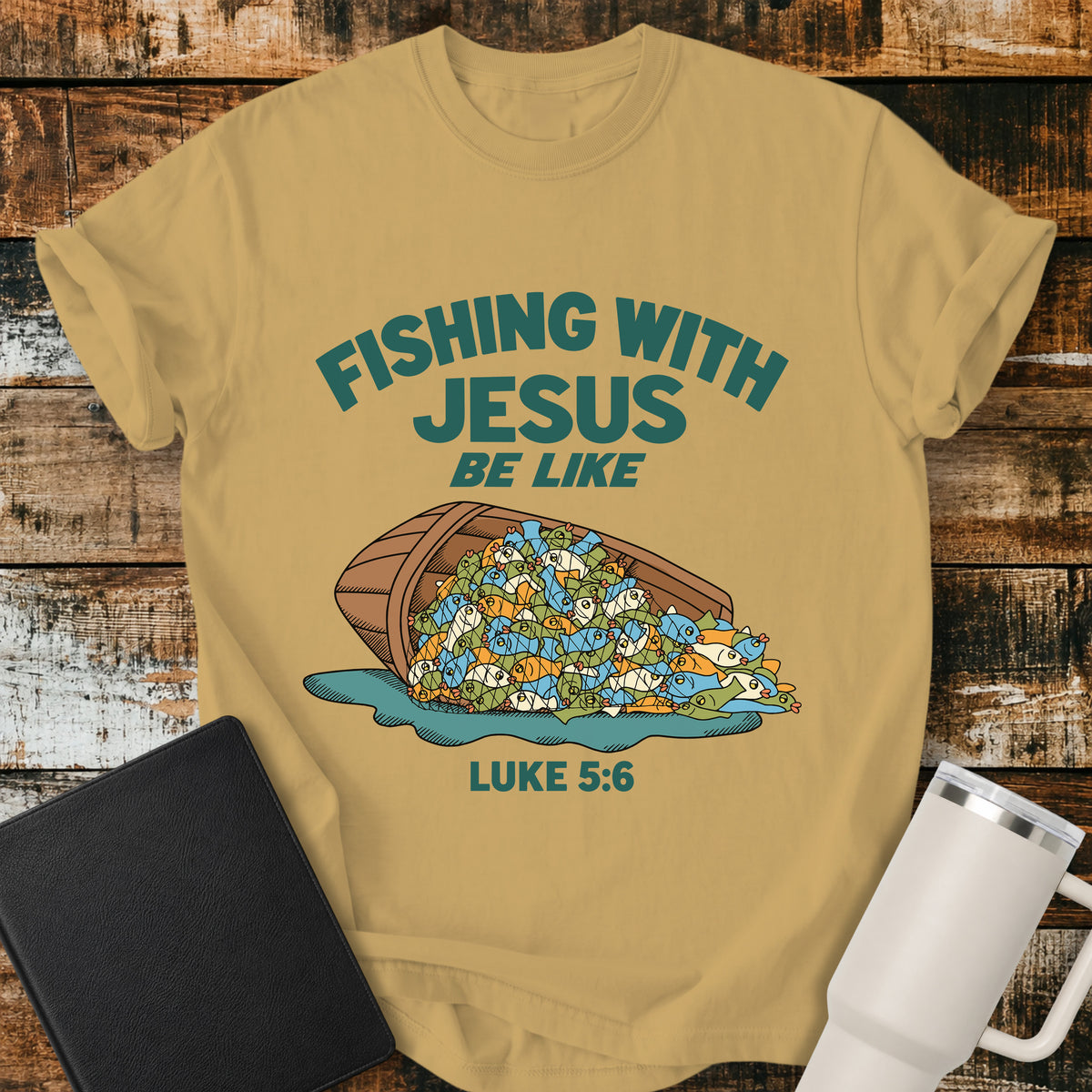 mustard yellow Christian t-shirt featuring a humorous overflowing catch of fish spilling from a boat, with bold retro text reading “Fishing With Jesus Be Like” and Luke 5:6.