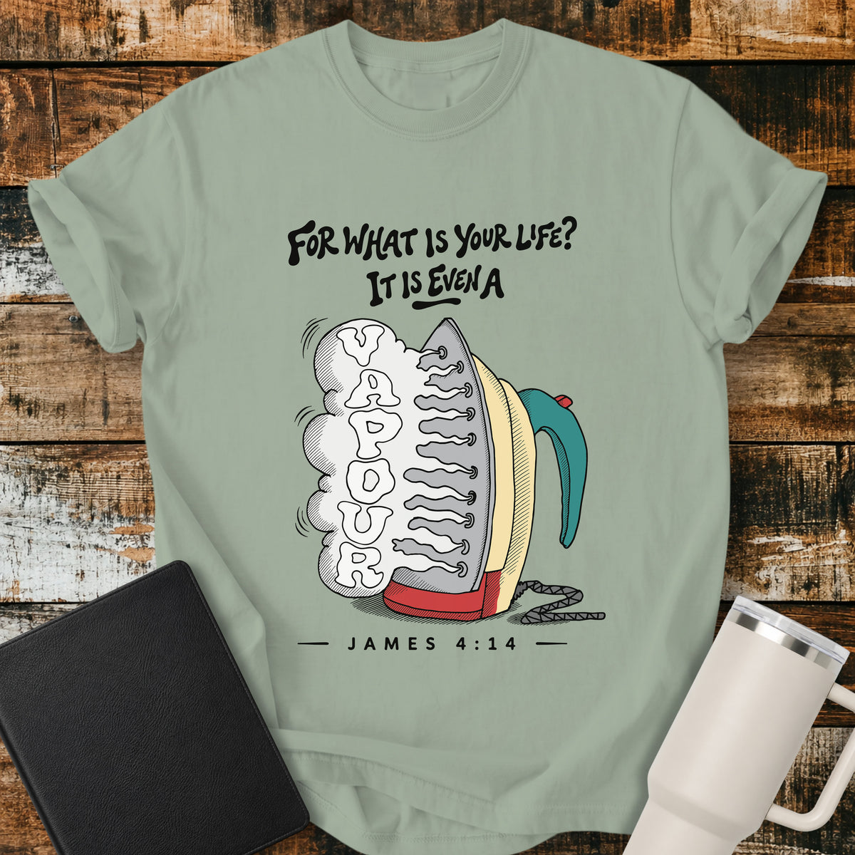 bay green flat-lay t-shirt mockup featuring a colorful vintage-style steam iron releasing a large cloud of steam shaped into the word "VAPOUR." Above the illustration, stylized lettering reads, "FOR WHAT IS YOUR LIFE? IT IS EVEN A," with the Bible reference "JAMES 4:14" below. The faith-inspired design is displayed on a rustic wood plank background alongside a black leather Bible and a white insulated travel mug.