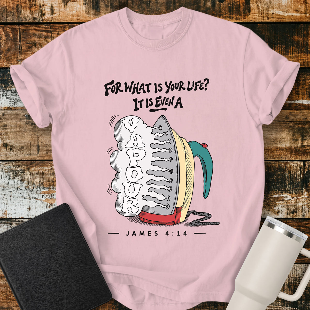 blossom pink flat-lay t-shirt mockup featuring a colorful vintage-style steam iron releasing a large cloud of steam shaped into the word "VAPOUR." Above the illustration, stylized lettering reads, "FOR WHAT IS YOUR LIFE? IT IS EVEN A," with the Bible reference "JAMES 4:14" below. The faith-inspired design is displayed on a rustic wood plank background alongside a black leather Bible and a white insulated travel mug.