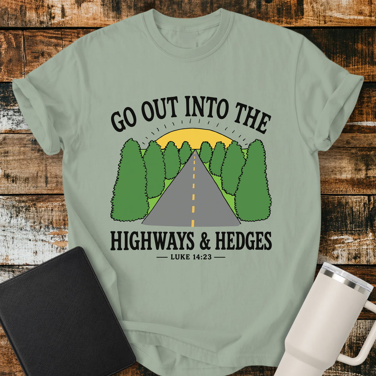 bay Christian t-shirt featuring a retro highway stretching through green hedges toward a sunrise, with the message “Go Out Into the Highways & Hedges” and the scripture reference Luke 14:23.