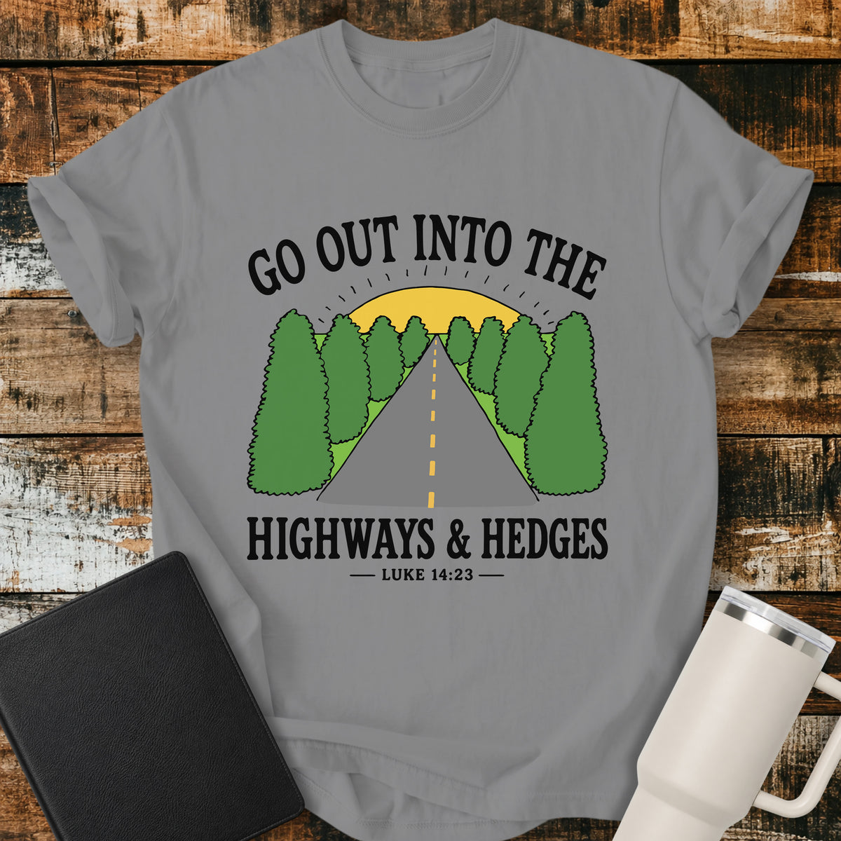 grey Christian t-shirt featuring a retro highway stretching through green hedges toward a sunrise, with the message “Go Out Into the Highways & Hedges” and the scripture reference Luke 14:23.