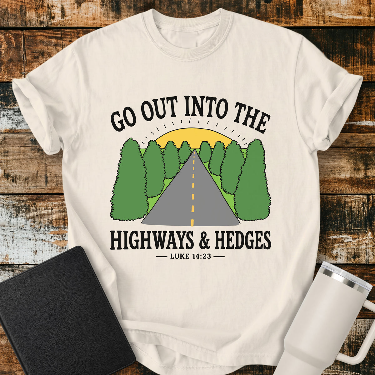 ivory Christian t-shirt featuring a retro highway stretching through green hedges toward a sunrise, with the message “Go Out Into the Highways & Hedges” and the scripture reference Luke 14:23.