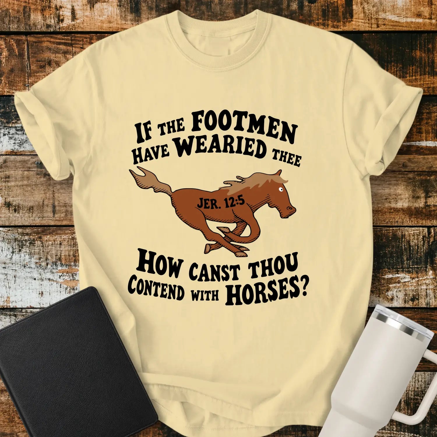 banana yellow graphic T-shirt mockup featuring a running horse illustration with the Bible verse phrase “If the Footmen Have Wearied Thee, How Canst Thou Contend with Horses?” and Jeremiah 12:5 reference, styled with a black Bible and white tumbler on a rustic wood background.