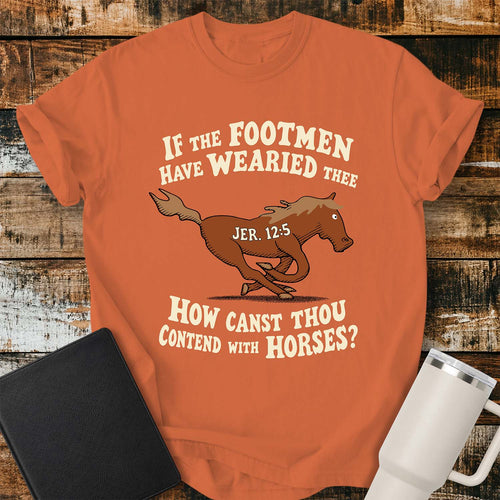 Burnt orange T-shirt featuring a running horse surrounded by the Bible verse, “IF THE FOOTMEN HAVE WEARIED THEE, HOW CANST THOU CONTEND WITH HORSES?” with “JER. 12:5” on the horse. The shirt is displayed on a rustic wood plank background alongside a black Bible and a white insulated tumbler.