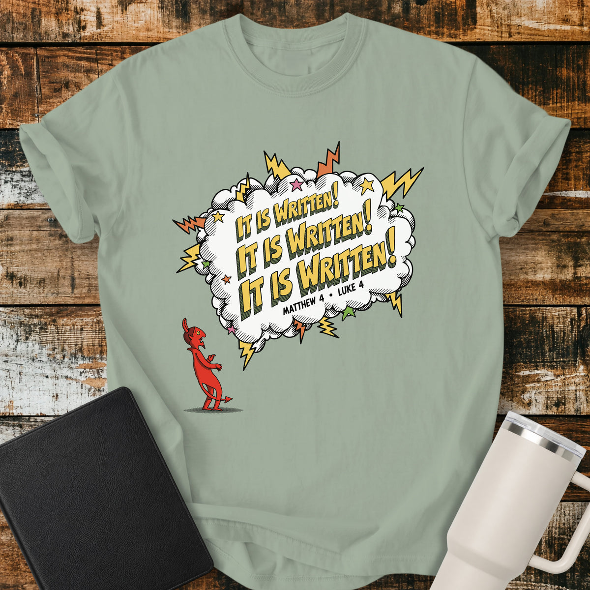 bay green Christian t-shirt featuring a comic-book-style burst with the words “It Is Written!” repeated three times, alongside a defeated devil character and references to Matthew 4 and Luke 4. A bold, playful biblical design inspired by Jesus answering Satan’s temptations with Scripture.