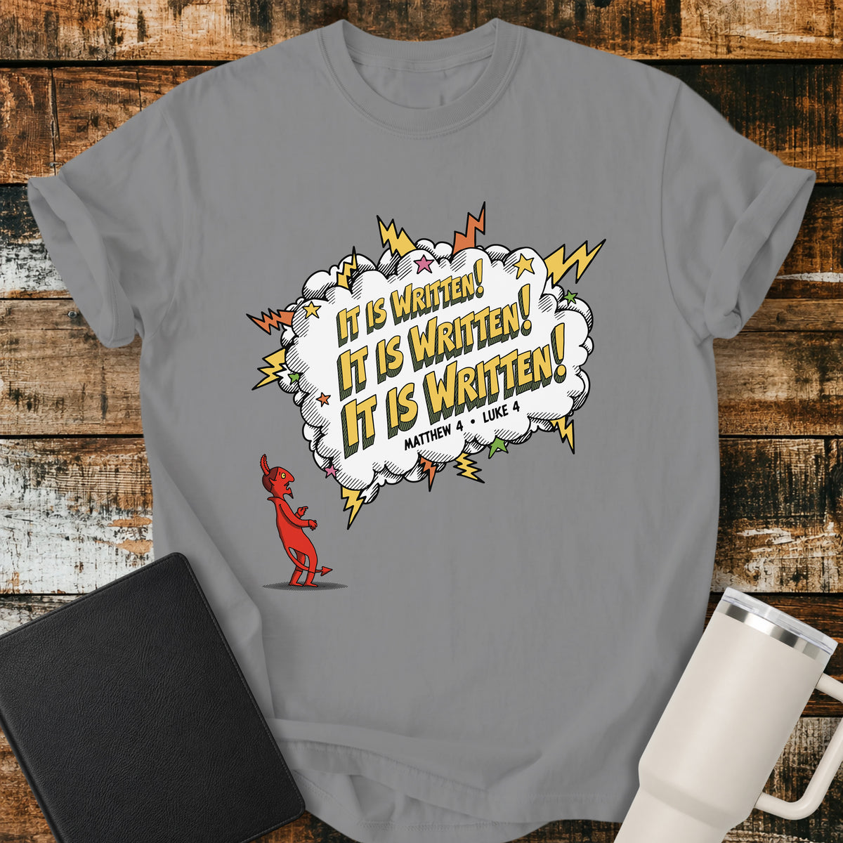 grey Christian t-shirt featuring a comic-book-style burst with the words “It Is Written!” repeated three times, alongside a defeated devil character and references to Matthew 4 and Luke 4. A bold, playful biblical design inspired by Jesus answering Satan’s temptations with Scripture.
