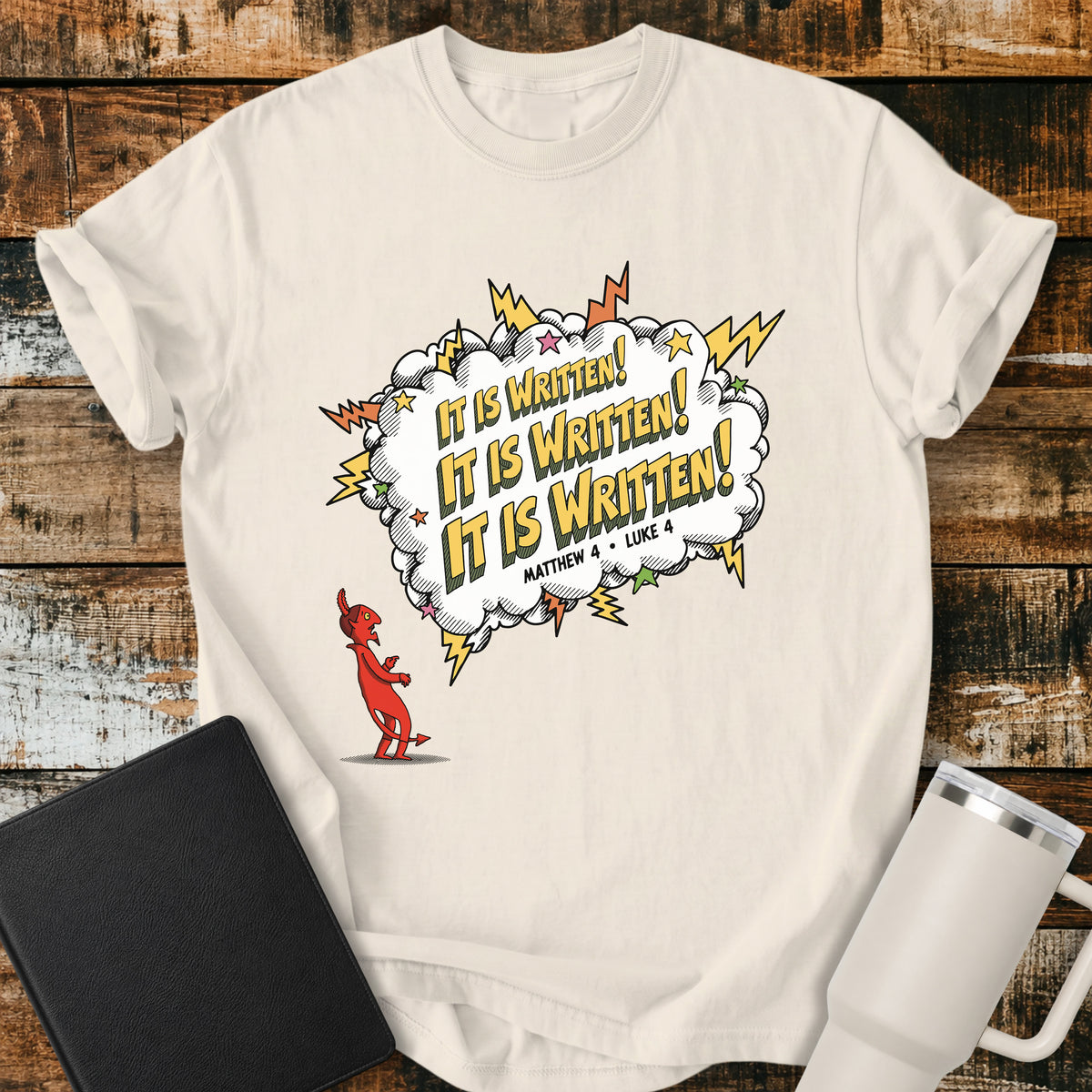 ivory Christian t-shirt featuring a comic-book-style burst with the words “It Is Written!” repeated three times, alongside a defeated devil character and references to Matthew 4 and Luke 4. A bold, playful biblical design inspired by Jesus answering Satan’s temptations with Scripture.
