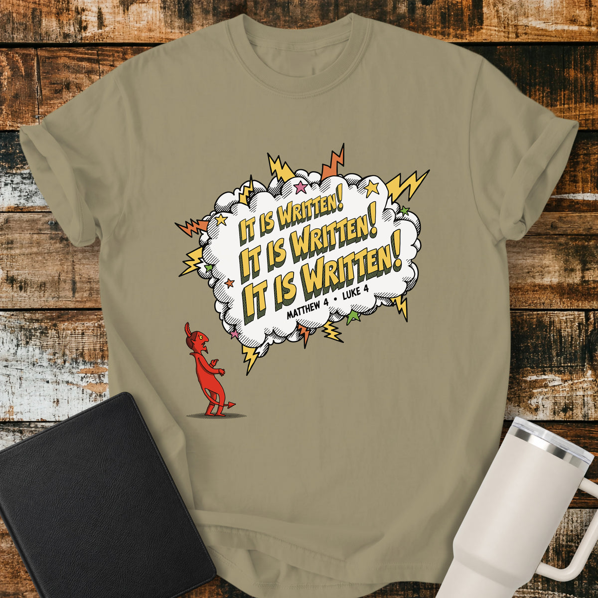 Khaki Christian t-shirt featuring a comic-book-style burst with the words “It Is Written!” repeated three times, alongside a defeated devil character and references to Matthew 4 and Luke 4. A bold, playful biblical design inspired by Jesus answering Satan’s temptations with Scripture.