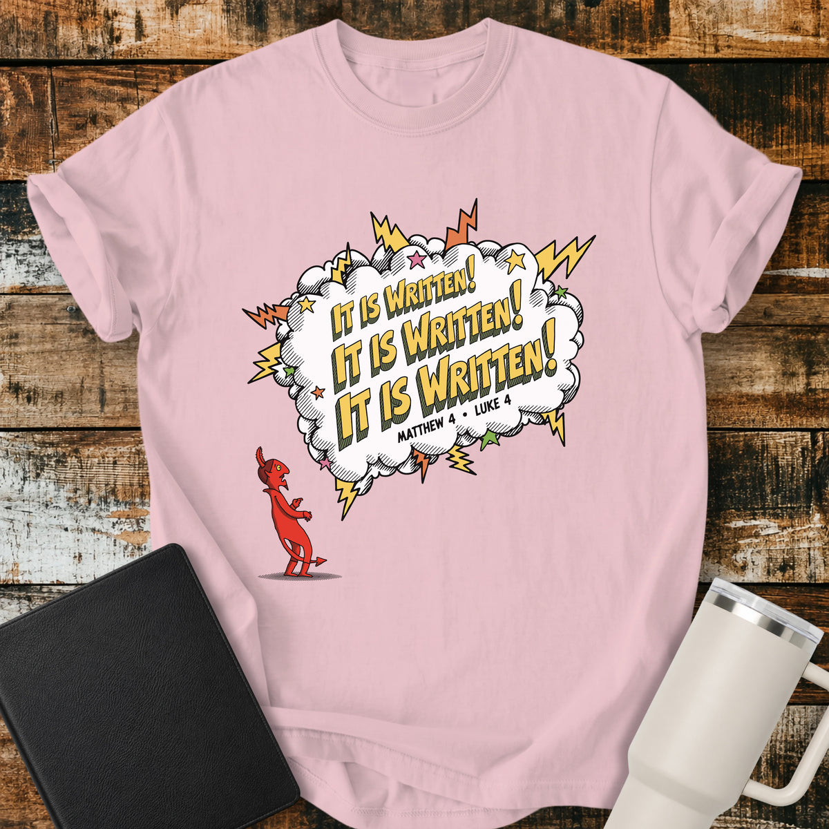 blossom pink Christian t-shirt featuring a comic-book-style burst with the words “It Is Written!” repeated three times, alongside a defeated devil character and references to Matthew 4 and Luke 4. A bold, playful biblical design inspired by Jesus answering Satan’s temptations with Scripture.