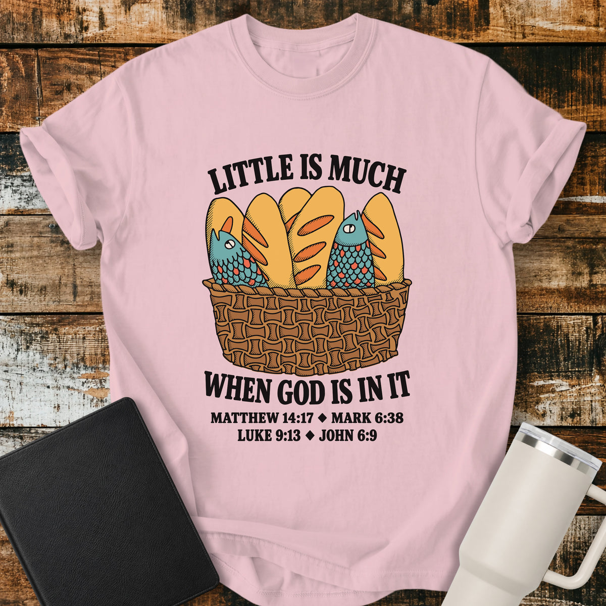 blossom pink Christian t-shirt featuring a vintage-style basket filled with five loaves and two fish, with bold lettering reading “Little Is Much When God Is in It” and references to Matthew 14:17, Mark 6:38, Luke 9:13, and John 6:9.