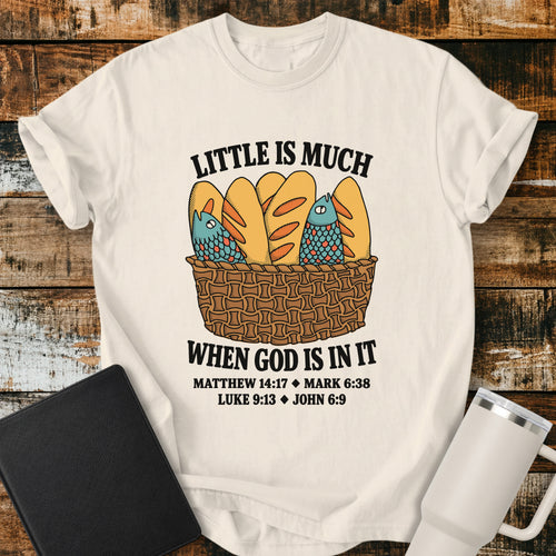 Ivory Christian t-shirt featuring a vintage-style basket filled with five loaves and two fish, with bold lettering reading “Little Is Much When God Is in It” and references to Matthew 14:17, Mark 6:38, Luke 9:13, and John 6:9.
