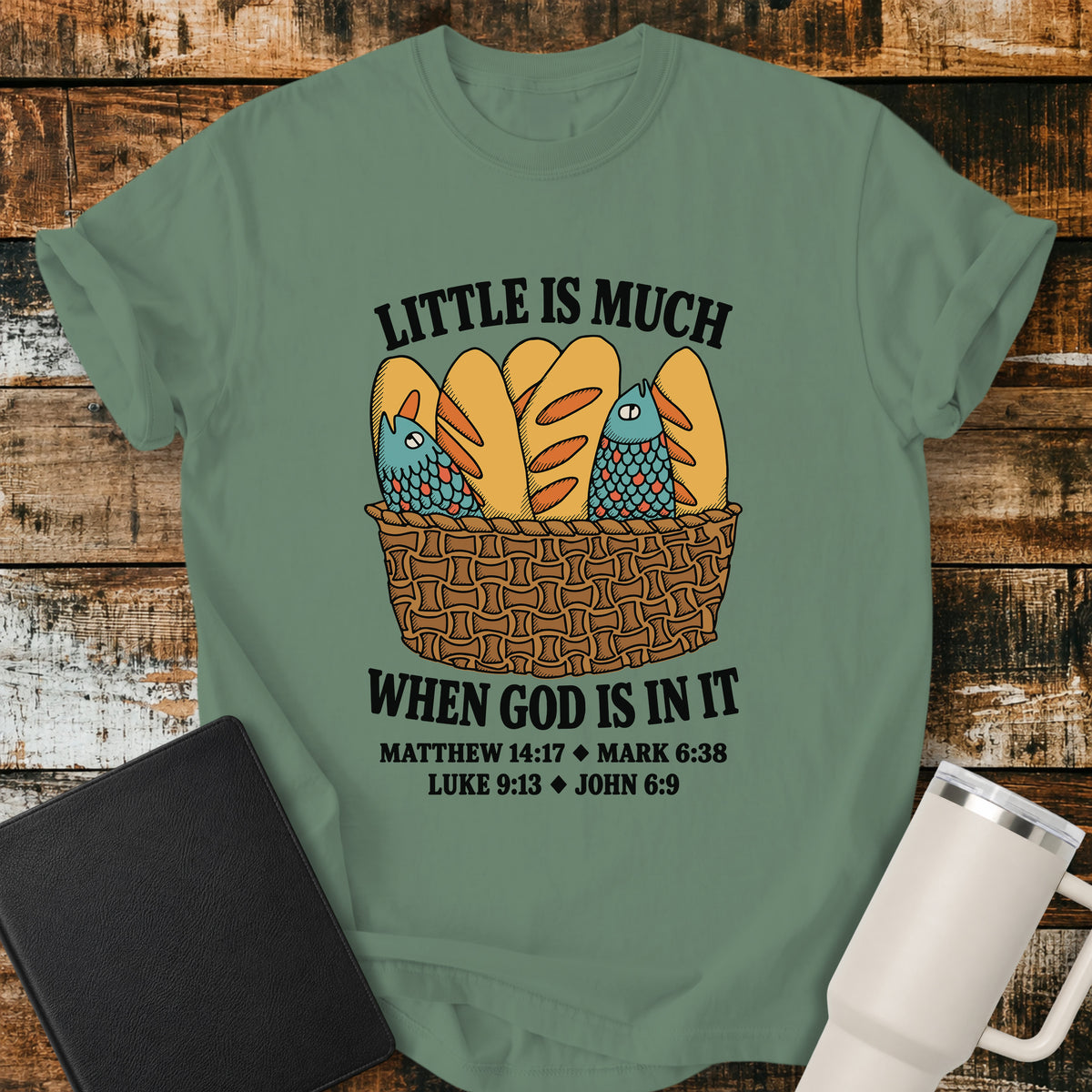 light green Christian t-shirt featuring a vintage-style basket filled with five loaves and two fish, with bold lettering reading “Little Is Much When God Is in It” and references to Matthew 14:17, Mark 6:38, Luke 9:13, and John 6:9.