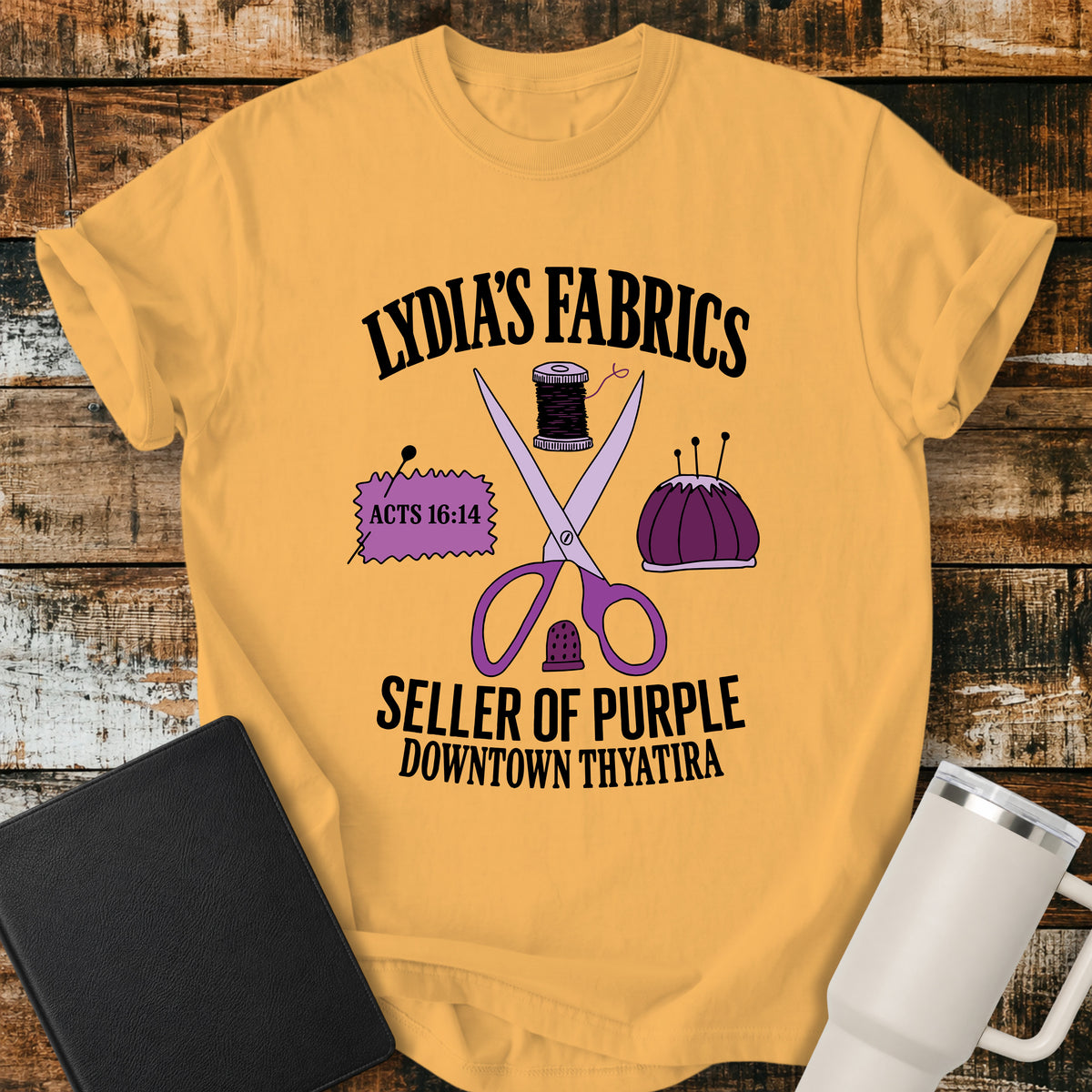 citrus yellow Christian t-shirt featuring vintage sewing notions—scissors, thread, pincushion, thimble, and fabric—with retro shop-style lettering reading “Lydia’s Fabrics,” “Seller of Purple,” “Downtown Thyatira,” and Acts 16:14.