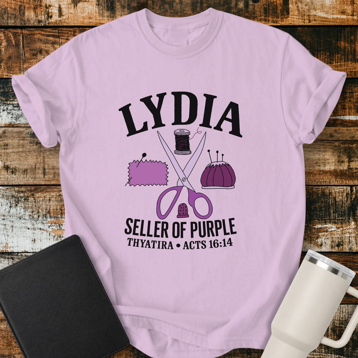 Orchid purple Christian t-shirt featuring vintage sewing illustrations including scissors, thread, fabric, pincushion, and thimble, with bold lettering reading “Lydia — Seller of Purple” and “Thyatira • Acts 16:14.”