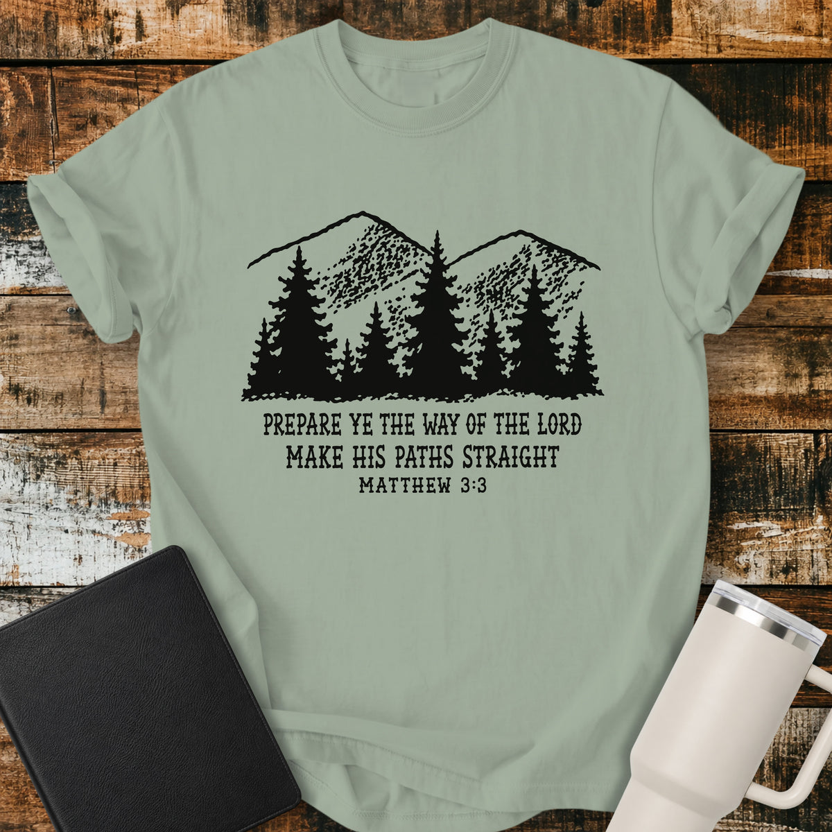 Bay green Christian t-shirt featuring a vintage mountain and pine forest illustration with the words “Prepare Ye the Way of the Lord, Make His Paths Straight” and Matthew 3:3. A rugged, outdoors-inspired biblical design with classic black typography.