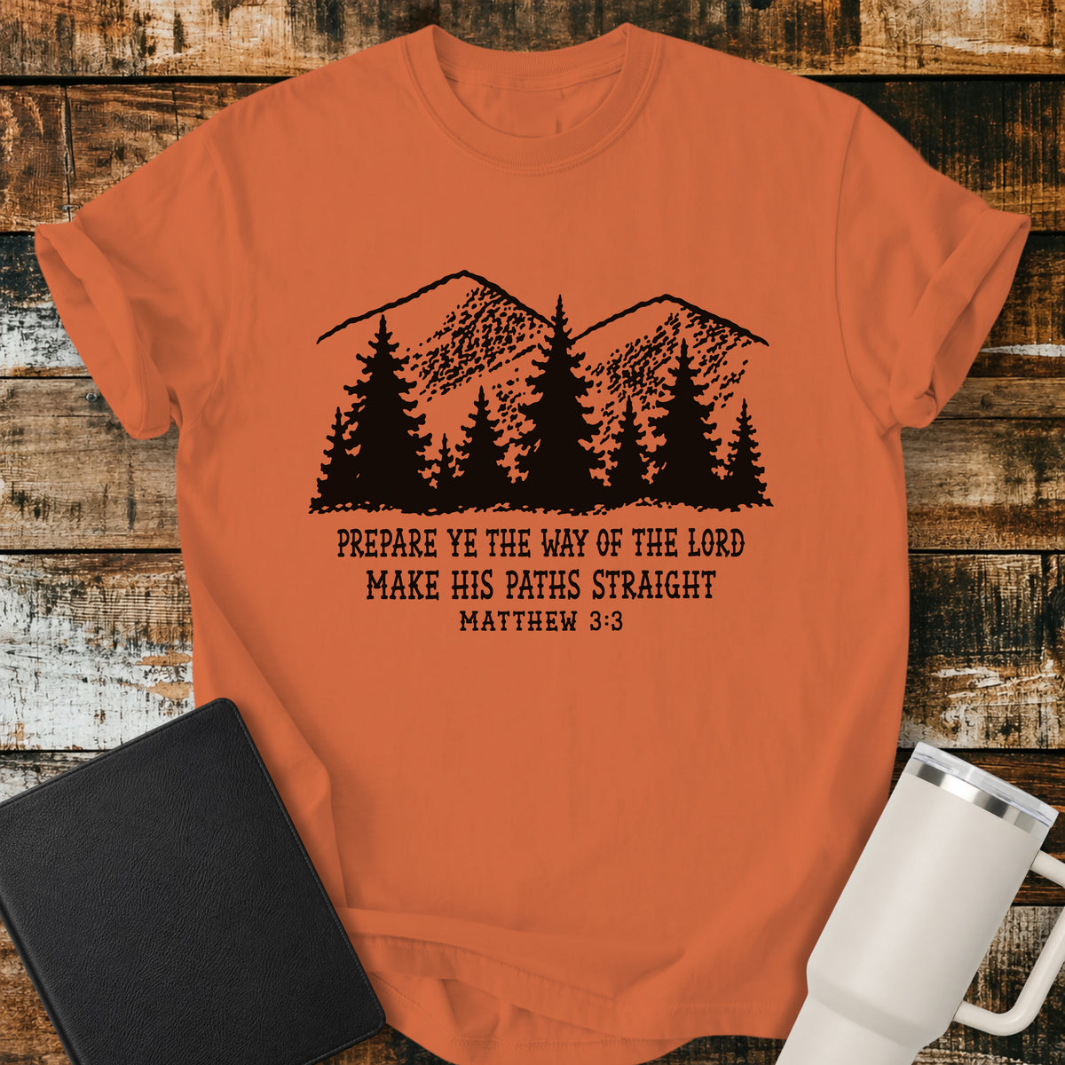 burnt orange Christian t-shirt featuring a vintage mountain and pine forest illustration with the words “Prepare Ye the Way of the Lord, Make His Paths Straight” and Matthew 3:3. A rugged, outdoors-inspired biblical design with classic black typography.