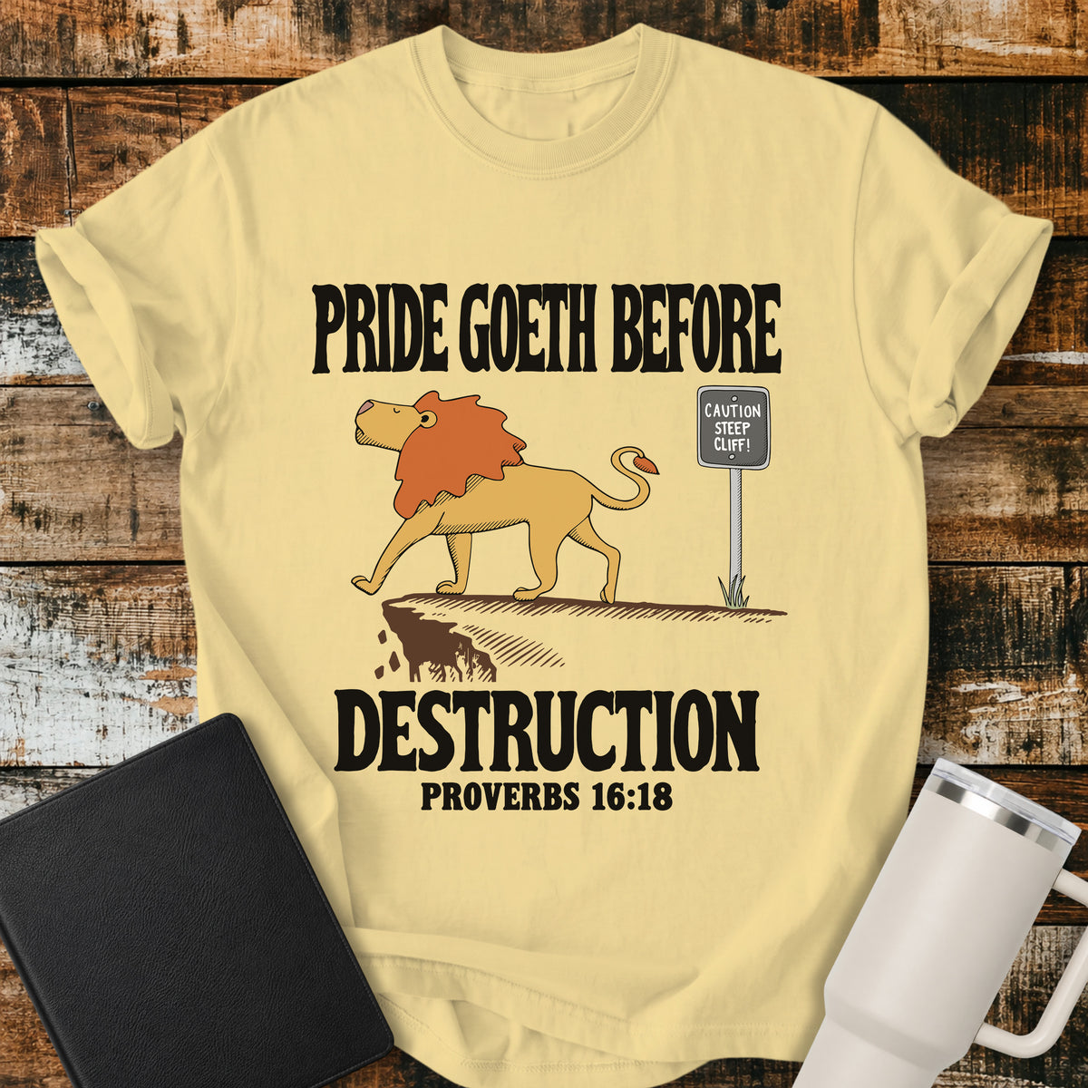 butter yellow Christian t-shirt featuring a lion confidently approaching a steep cliff, with bold vintage lettering reading “Pride Goeth Before Destruction” and Proverbs 16:18.