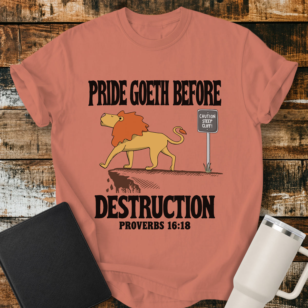 terracotta Christian t-shirt featuring a lion confidently approaching a steep cliff, with bold vintage lettering reading “Pride Goeth Before Destruction” and Proverbs 16:18.