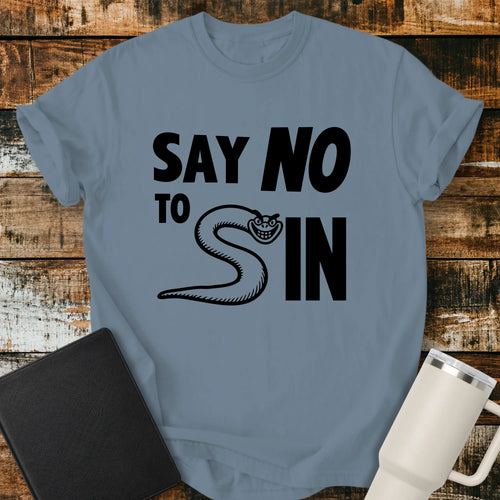 ice blue T-shirt mockup featuring the phrase “SAY NO TO SIN” in bold black lettering, with a smiling snake cleverly forming the letter “S” in the word “SIN.” The minimalist Christian-themed design is centered on the shirt. The shirt is displayed on a rustic wood plank background beside a black Bible and a white insulated tumbler.