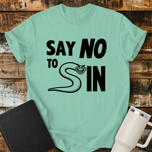 Island Reef green T-shirt mockup featuring the phrase “SAY NO TO SIN” in bold black lettering, with a smiling snake cleverly forming the letter “S” in the word “SIN.” The minimalist Christian-themed design is centered on the shirt. The shirt is displayed on a rustic wood plank background beside a black Bible and a white insulated tumbler.